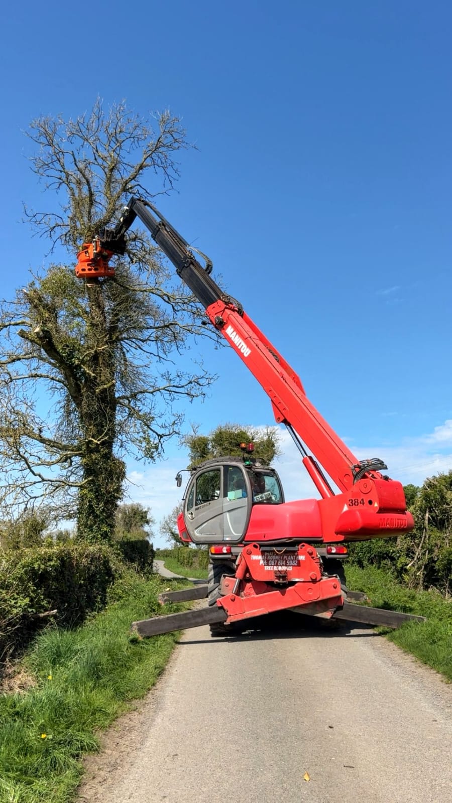 Manitou telehandler with grapple attachment lifting a section of tree on a narrow rural lane in Co. Meath